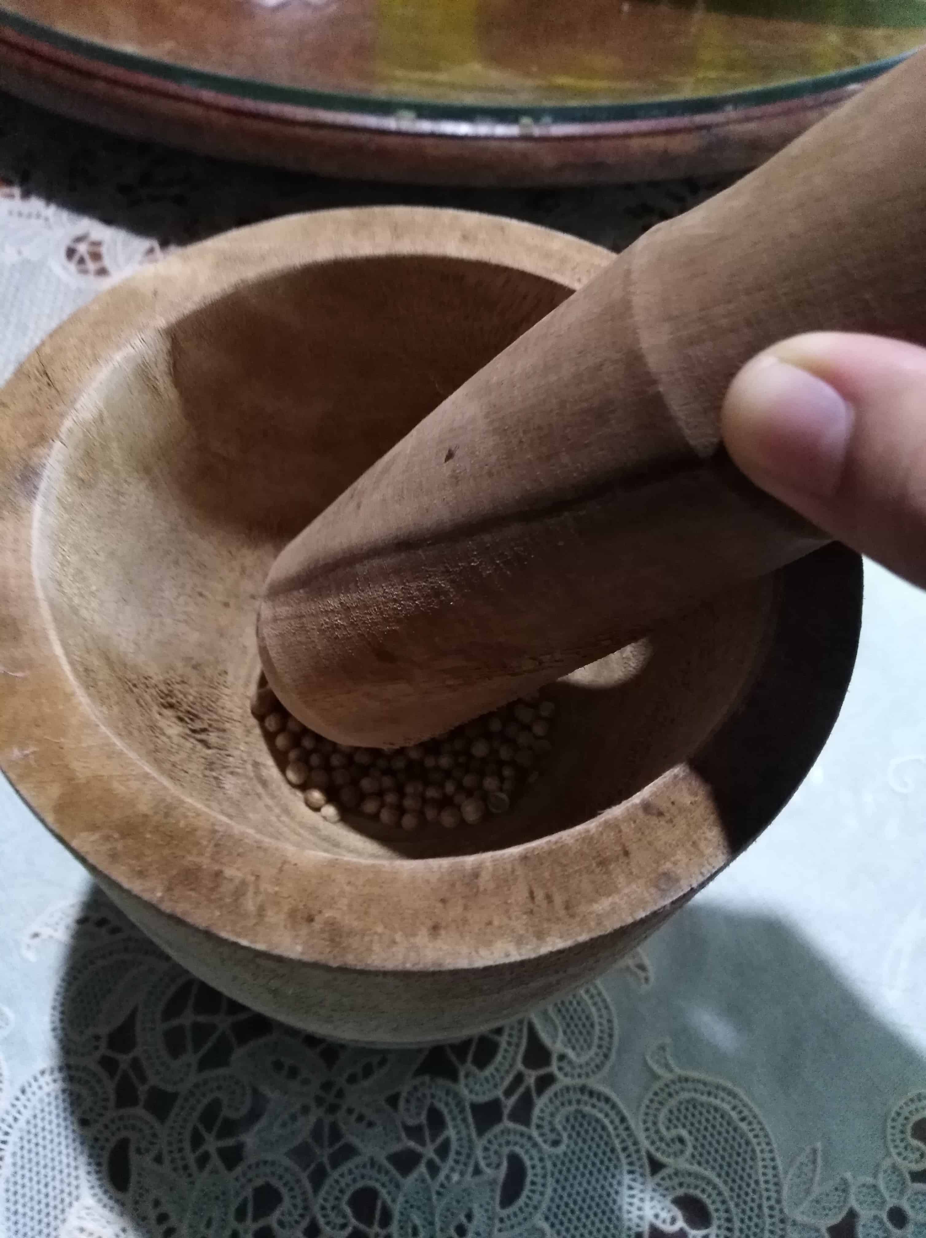 Crushing whole coriander seeds in a mortar with a pestle