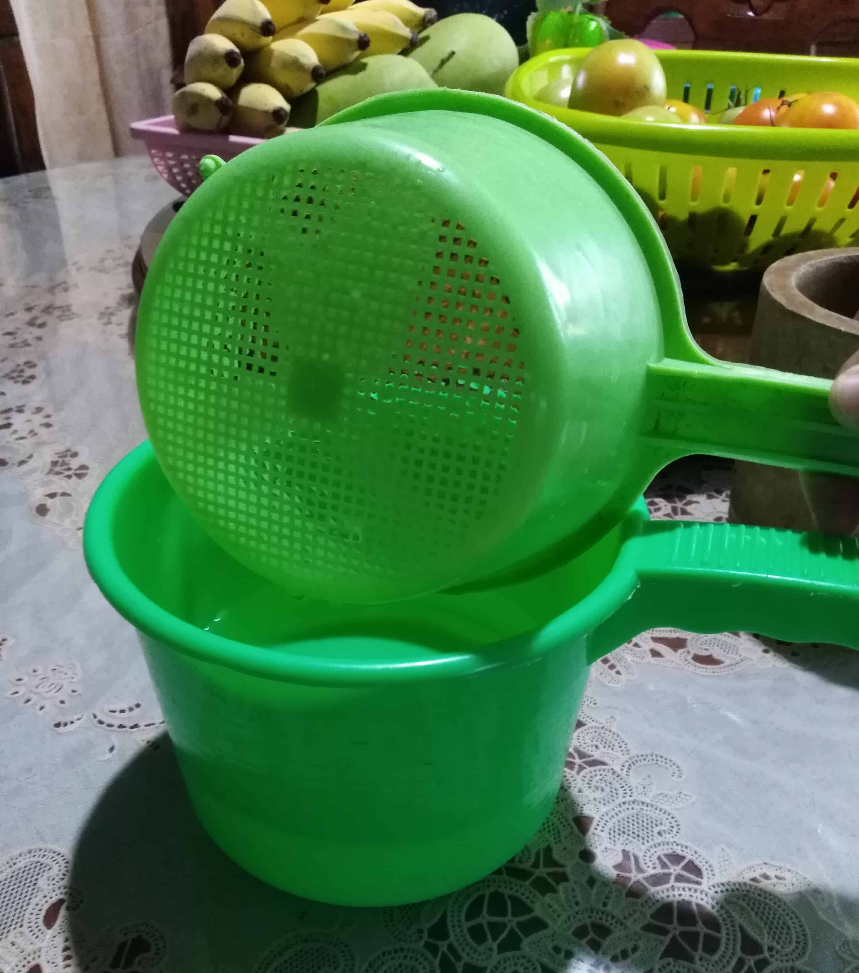 A small green colander placed on top of a green dipper/ladle/water scooper